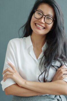 Photo by Vitaly Gariev Portrait of a confident young woman smiling with folded arms, wearing glasses and a white shirt.