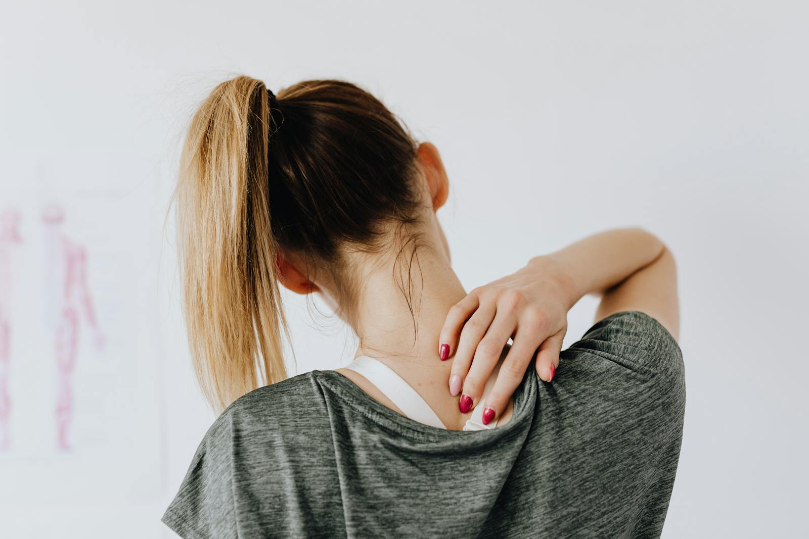 Photo by Karola G A woman in casual clothing holds her neck, indicating pain or discomfort.