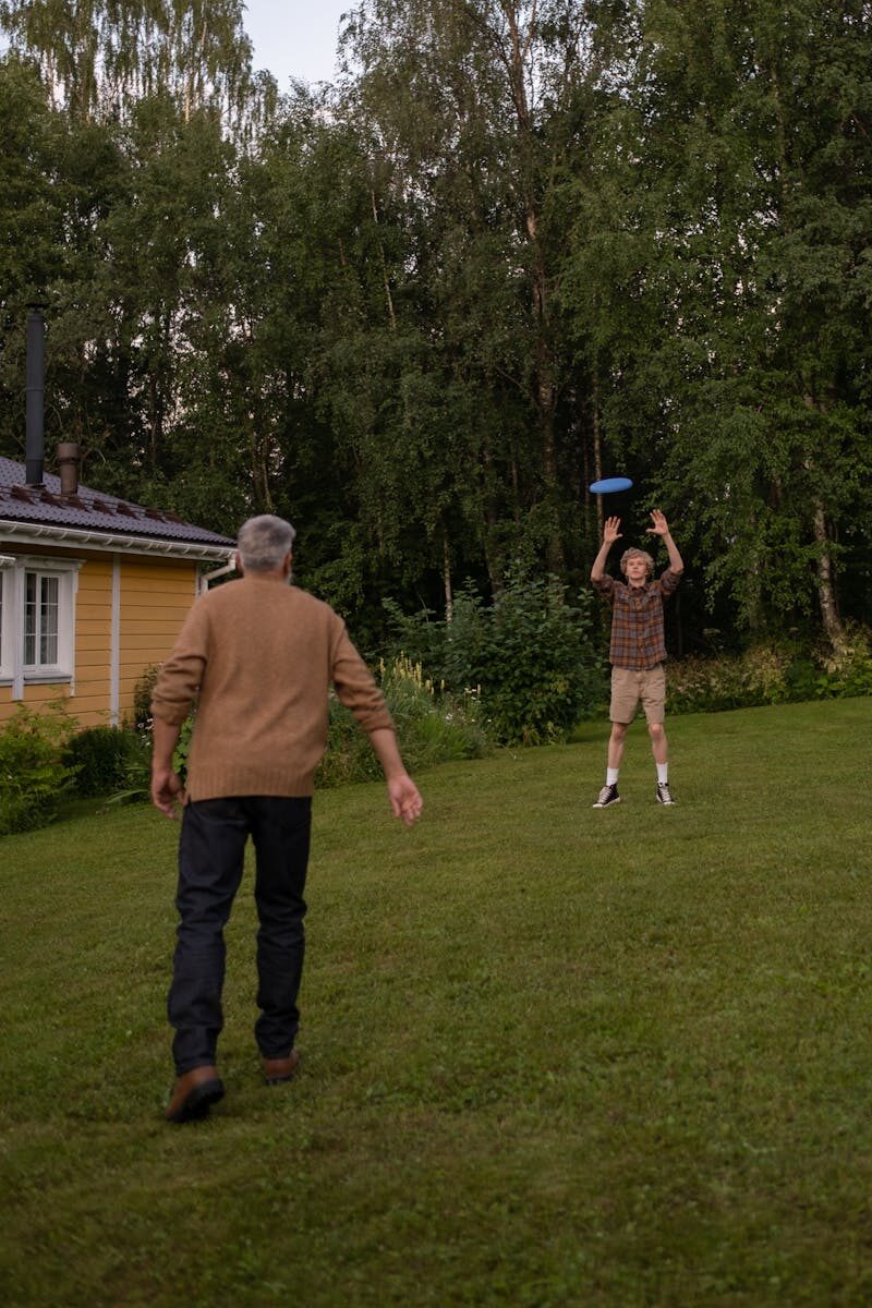Elderly man and young boy enjoying a game of frisbee in a grassy backyard.