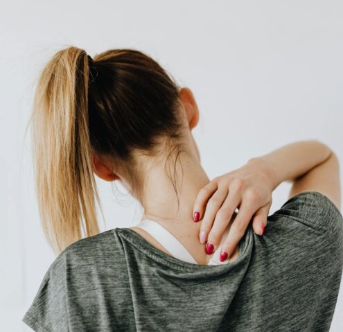 A woman in casual clothing holds her neck, indicating pain or discomfort.