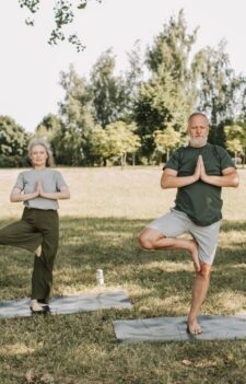 An elderly couple doing yoga in a serene park setting, promoting a healthy lifestyle.